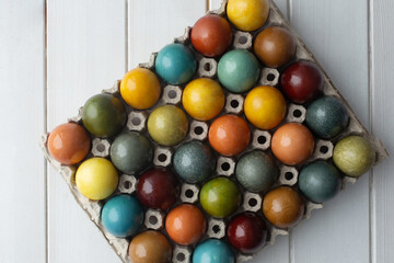 Set of colorful easter eggs colored with natural dye in cardboard on white wooden background