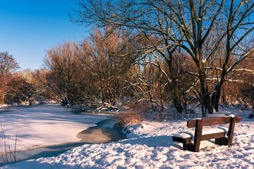verschneite Park Bank mit Blick auf den vereisten Fluss