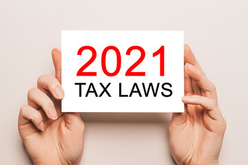 Female hands hold card paper with text 2021 tax laws on a yellow background. Business and finance concept