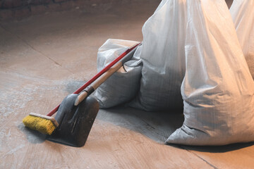 Shovel, broom and bags with a construction garbage on the dusty construction site floor background.