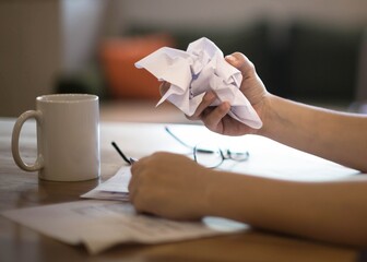 A frustrated discouraged woman crumpling a paper at work on her desk.