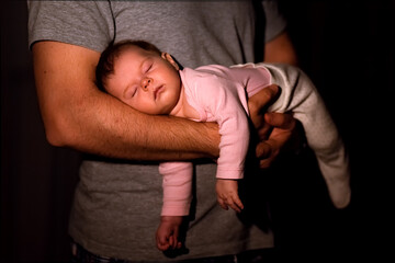 cute baby 0-2 years old sweetly sleeps belly down on the beautiful athletic arms of dad at night indoors, the baby is calm and relaxed