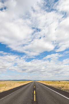 Open road disappears to vanishing point under a perfect broken cloud sky and past dry grasslands in Grant County in Washington State