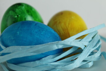 Three colored blue yellow green eggs lie in the nest on a white background with a place to text a copyspace view from the side of Von Easter