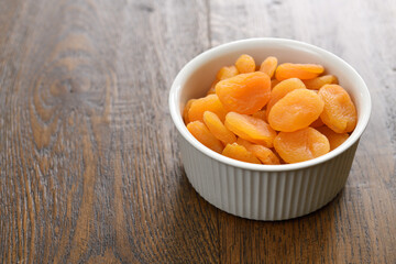 Dried apricots in a ceramic bowl on stained hickory wood planks