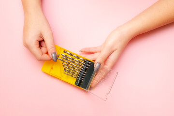 a woman's hand pulls a drill bit out of the box. pink background