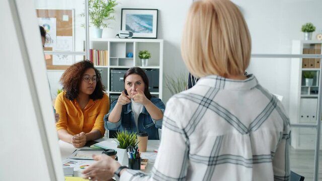 Active initiative women are talking to female speaker making presentation pointing at board in office discussing work together. People and discussion concept.