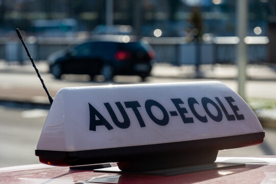 Panneau écrit en Français "auto-école" fixé sur le toit d'une voiture. Automobile circulant à l'arrière-plan