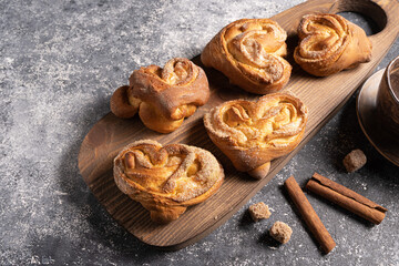 The heart-shaped sugar-sprinkled buns, made at home, are laid out on a wooden board, along with pieces of brown sugar and vanilla sticks. Close-up, copy space..