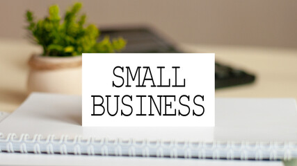 Paper card with text SMALL BUSINESS. Calculator, flowers and brown background