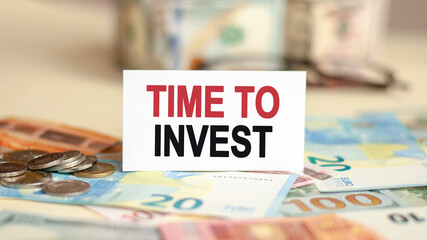 On the table are bills, a bundle of dollars and a sign on which it is written - TIME TO INVEST. Finance and economics concept.