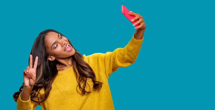 Portrait of cool cheerful African American student girl having video-call or taking selfie, holding smart phone in hand shooting selfie on front camera isolated  