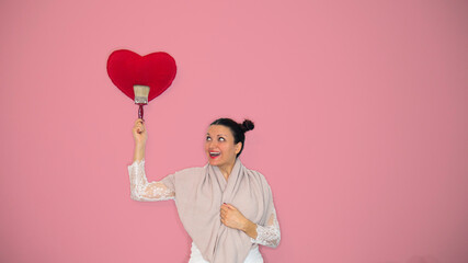 A smiling woman with a big brush draws a heart on the wall.