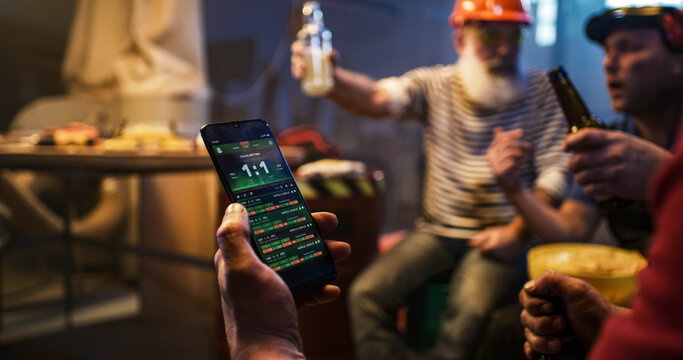 Men with smartphone watching match on tablet with friends