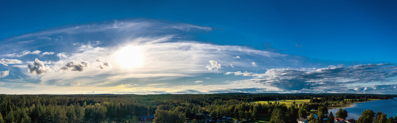 Breathtaking Aerial Panorama on Northern Scandinavian landscape with much pine tree and spruce forests. Big forest to horizon line, lake, bright Sun in blue scenic summer skies. Umea, Northern Sweden