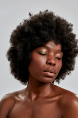 Close up portrait of adorable african american young woman with afro hair and perfect smooth glowing skin looking down, posing isolated over gray background