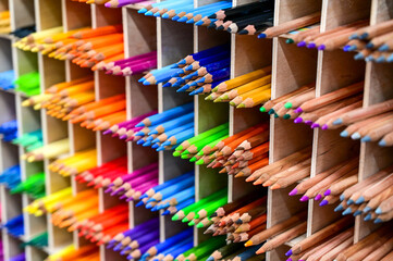 Bright multicolored pencils on the wooden shelves at the shop. Different colored pencils background. Selective focus. 