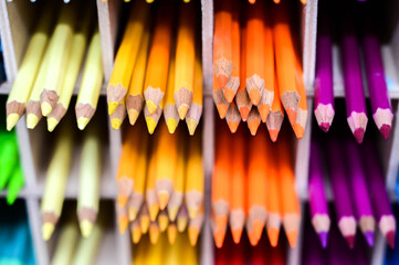 Bright multicolored pencils on the wooden shelves at the shop. Different colored pencils background. Selective focus. 