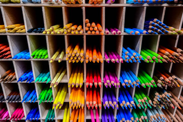Bright multicolored pencils on the wooden shelves at the shop. Different colored pencils background. Selective focus. 