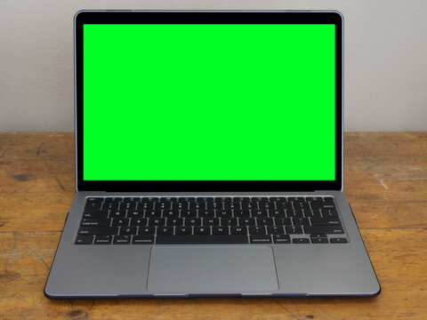 A modern laptop computer is shown isolated on an old, wood office desk, with a green screen on the monitor to add your own graphics.