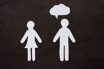 The silhouettes of a man and woman in a dress made of white paper, cut by hand. With speech-bubble over man. On black background