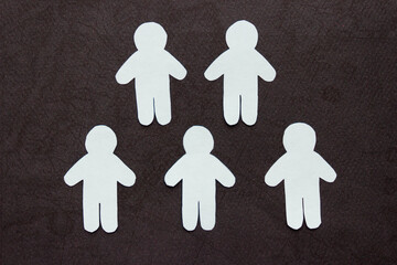 Silhouettes of five people cut from white paper. On black background. Group of people. Teamwork, communication, togetherness, friendship