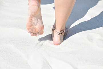 Young girl walking on the beach barefoot. Tiny woman feet on the white sand with the anklet of multicoloured threads.