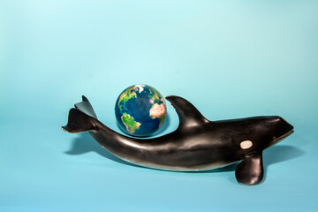 plastic toy orca whale and planet earth on blue background