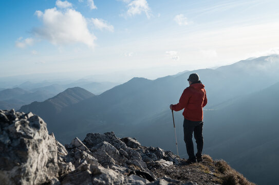 Young hiker Man standing with trekking poles on cliff edge and looking at Tatra mountains valley. Successful summit concept image.
