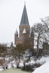 Fototapeta na wymiar Pointy rooftop tower with cants in winter wonderland landscape part of historic city center of medieval Hanseatic town during a snowstorm