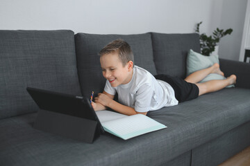 Online education, homeschooling. School boy having online lesson at home on the coach