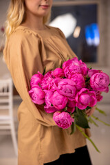 A mono-bouquet of peonies in the hands of a young florist girl in a bright loft-style room. Professional florist work. Vertical photo