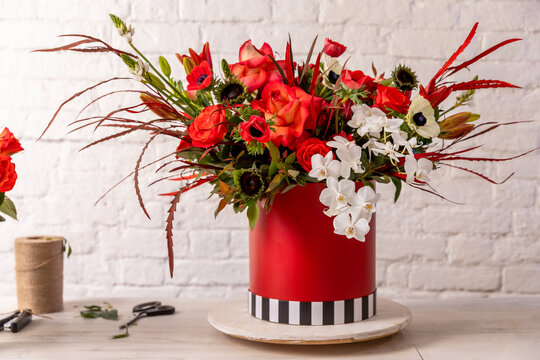 Floral arrangement in red shades of orchids, roses, sunflowers, lilies, alstroemerias and ornithogalums in a red box against a white brick wall. Professional florist work