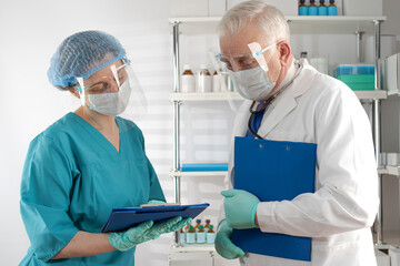 Doctor senior man in white coat and female paramedic examine documents in blue clipboard folder and discussing in the hospital