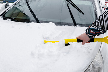 Man scraping snow from hood of car with brush. Person cleaning fresh snow after snowstorm from car in the winter close up.
