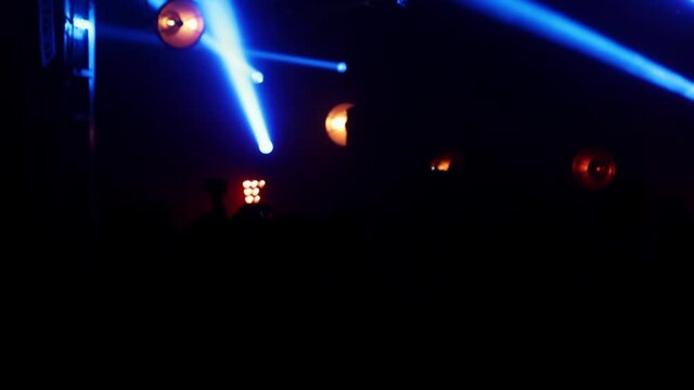 Concert crowd point of view inside a large concert hall during a music festival, the lit stage is visible. Light show and people dancing at a Dance Event.
