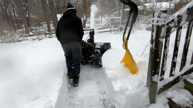 young man cleaning the driveway with a snow blower after the snow storm