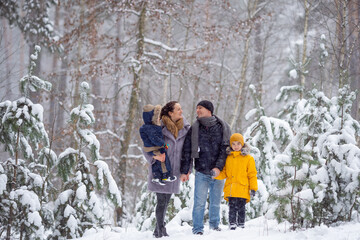 Family walking in winter park together. Adult man, woman and two children stroll surrounded by...