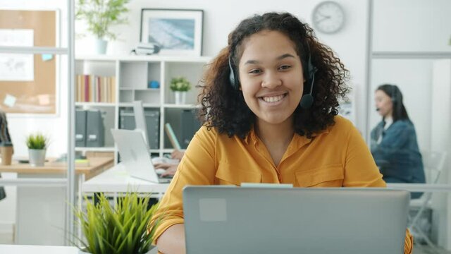 Slow motion portrait of happy African American girl call center worker smiling looking at camera in office. Communication and profession concept.