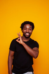 young handsome african american guy student posing cheerful and gesturing on yellow background, lifestyle people concept