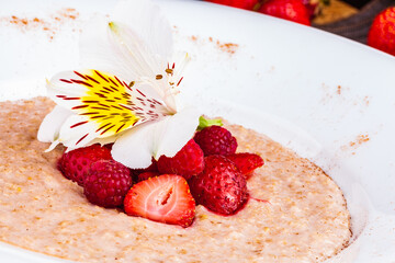 Oatmeal porridge with strawberries and raspberries in a white plate. Healthy food