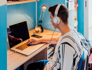 Teen studying with laptop and headphones in his room. Concept online class.