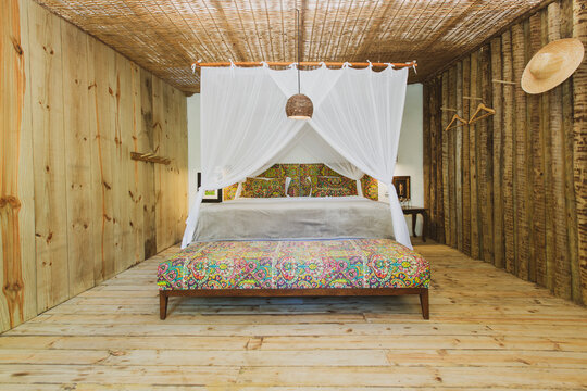 Modern luxury summer holiday or vacation wooden beach house bedroom interior with rustic canopy bed, sofa and straw chandelier. Detail of a hanging hat on the wall.