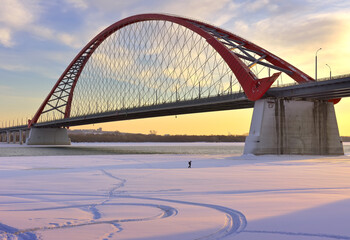 Winter morning on the Ob. A small man under the arch of the Bugrinsky automobile bridge on the bank of a frozen river in Novosibirsk