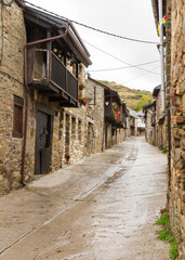 Fototapeta na wymiar Main Street El Acebo on the Camino de Santiago in the province of Leon in Spain, with buildings of stone and wooden balconies decorated with geraniums, a rainy day 