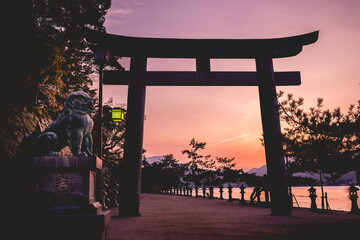 Amazing view of torii gate, lion sculpture and sunset over the sea with mountains in the horizon from the Miyajima Island, Japan