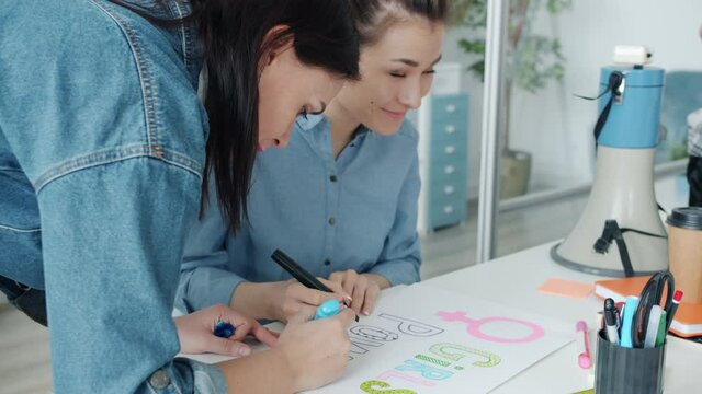 Slow motion of ambitious feminists Asian and Caucasian drawing posters for equal gender rights protest concentrated on creative activity indoors in office.