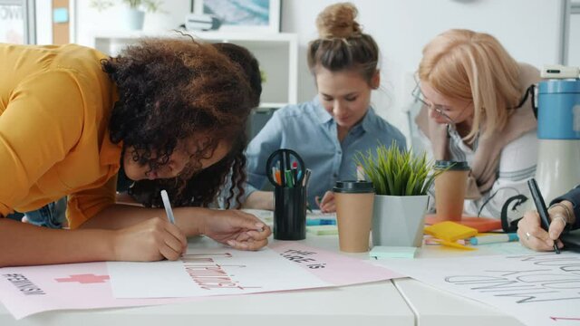 Slow motion of cheerful mixed race women making posters about feminism and talking enjoying creative activity together. Sisterhood and social activism concept.