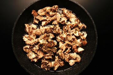 Pieces of meat fried in a frying pan. Top view. Dimmed light