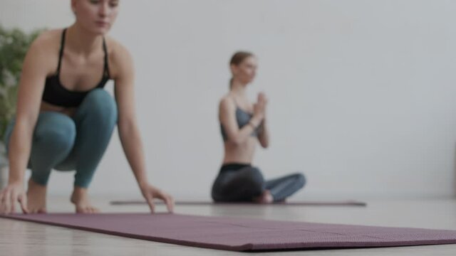 Lockdown of young Caucasian woman wearing sportswear unrolling yoga mat and getting ready for yoga practice